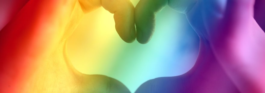 Hands in the shape of a heart with a rainbow filter for Pride month.
